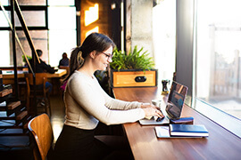 A close-up of a Content Writer working on a table with her laptop inside a cafe.